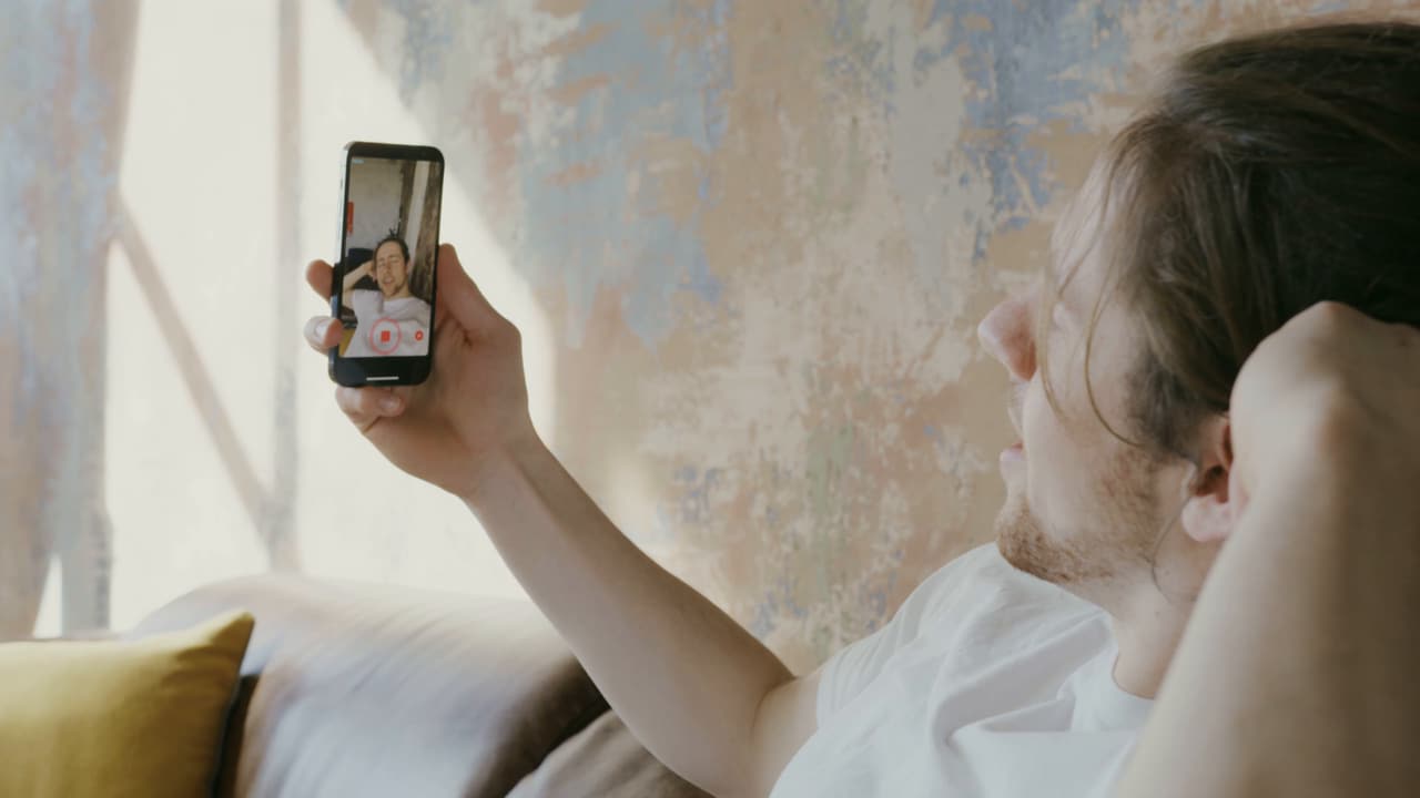 A man on a video call, holding his phone up and smiling at the person on screen